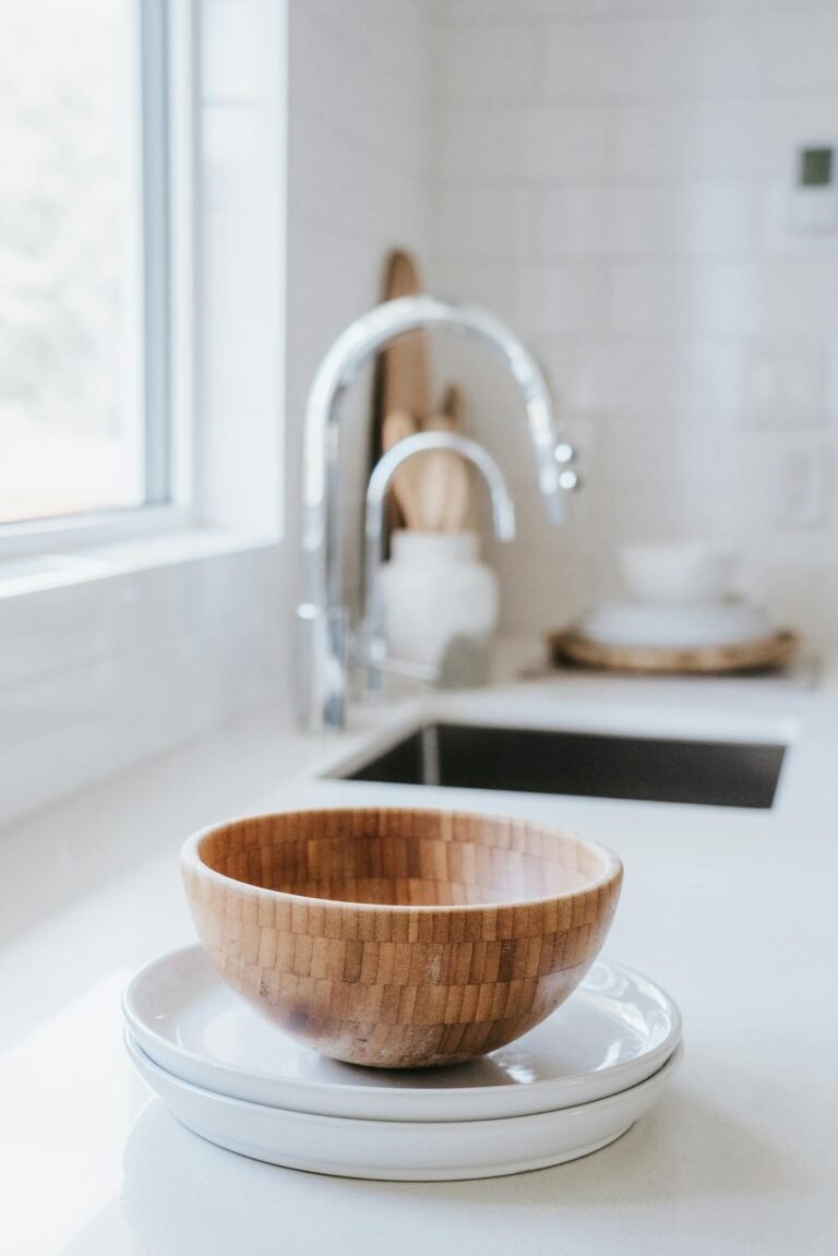 Bright minimalist kitchen scene with wooden bowl and plates near sink.