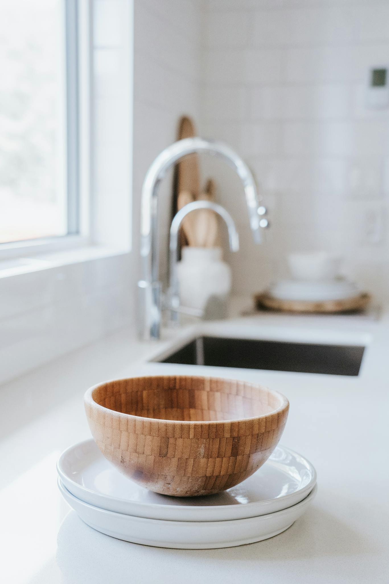 Bright minimalist kitchen scene with wooden bowl and plates near sink.
