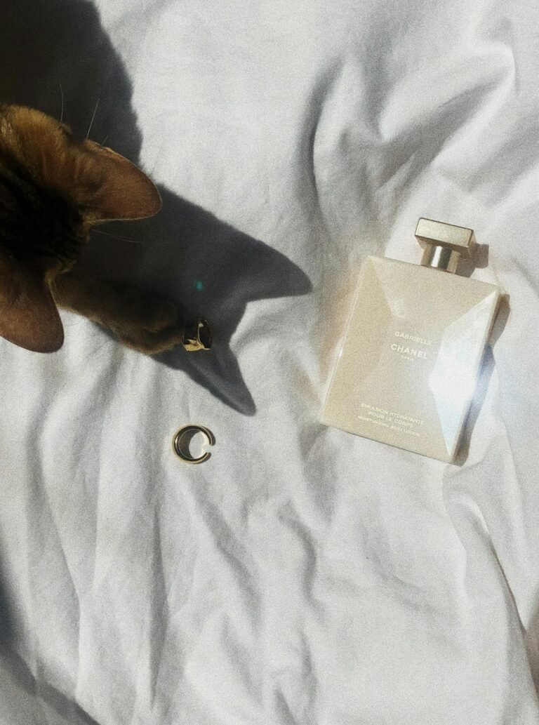 Chic composition featuring perfume bottle, cat, and shadow on white linen for a stylish touch.