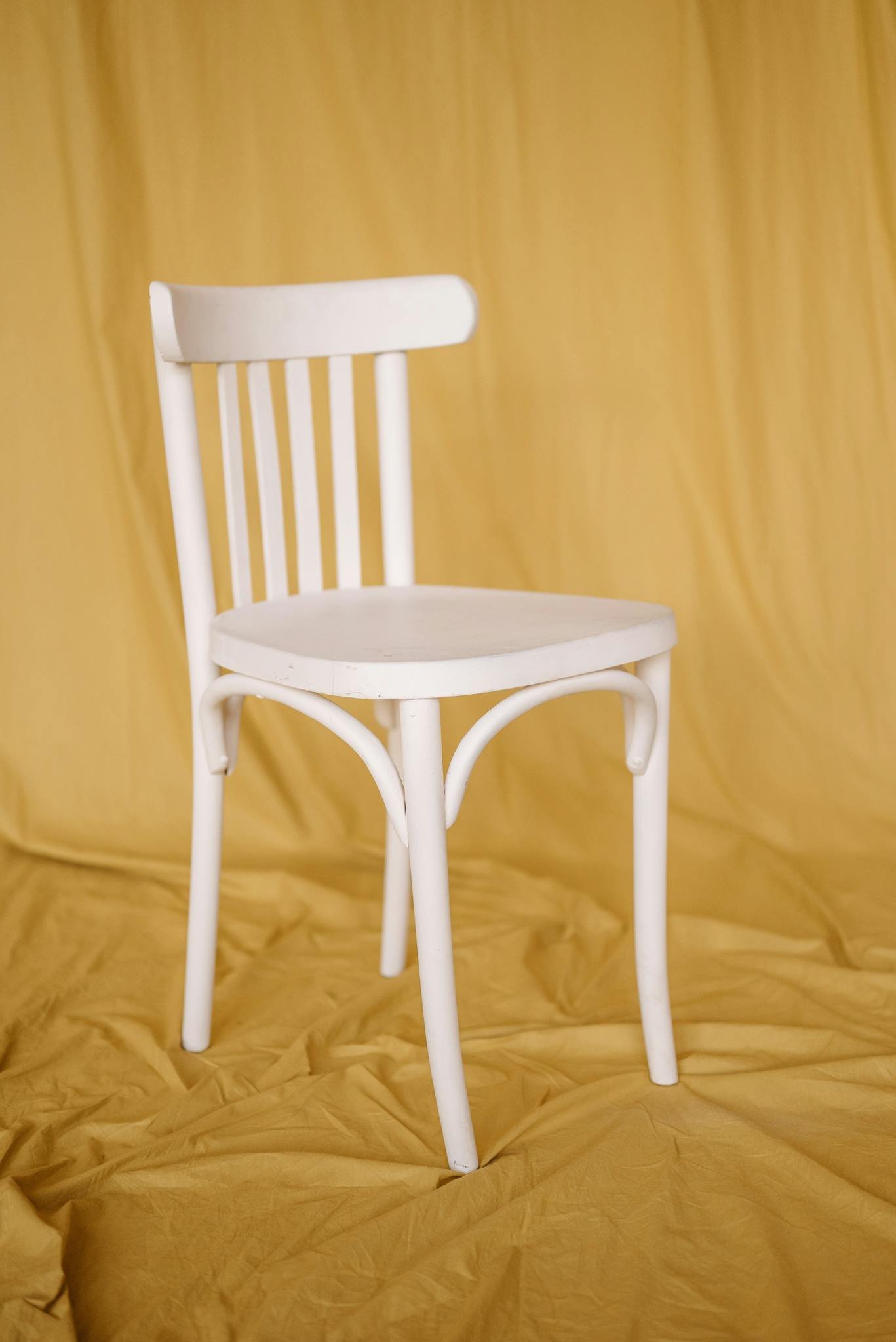 White wooden chair against a soft mustard backdrop in a minimalist studio setting.